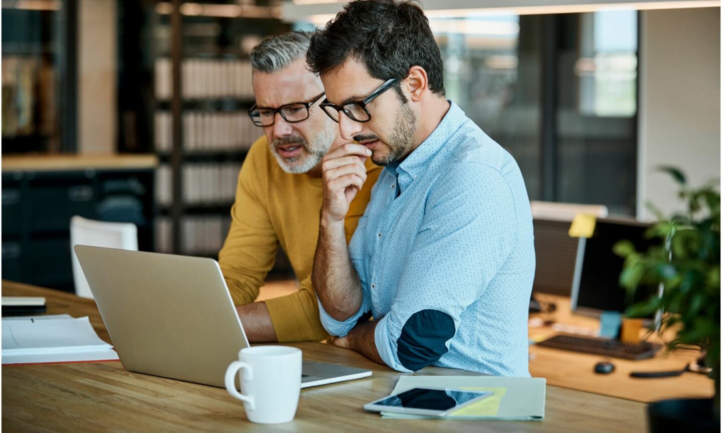 Two men in a meeting, sharing a laptop screen