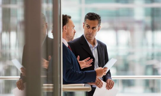 two business men having a discussion in an office while holding a tablet