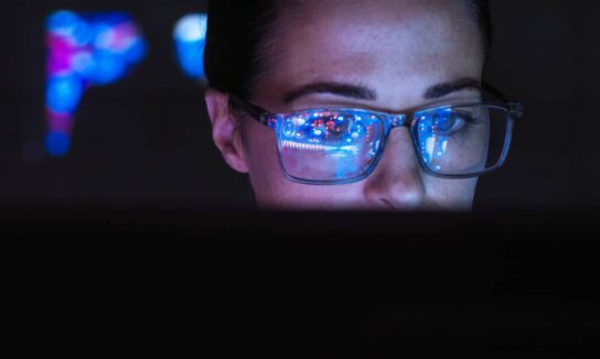 woman-in-glasses-using-a-computer-in-a-dark-room-with-reflections-of-the-screen-on-her-glasses